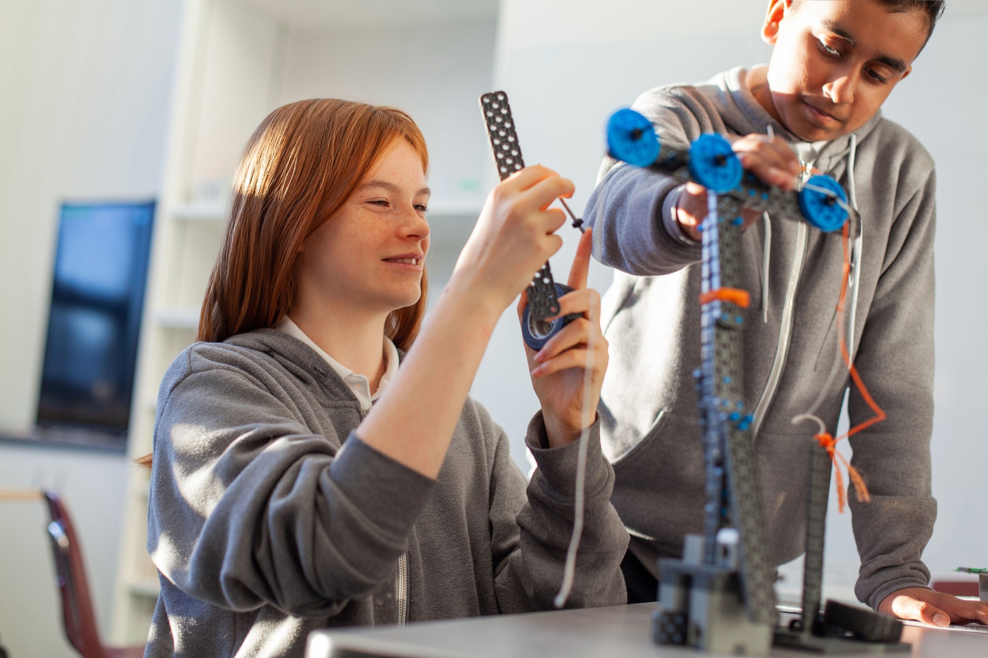 Teenage girl in high school classroom making physics construction science engineering technology mathematics STEM project with Asian classmate