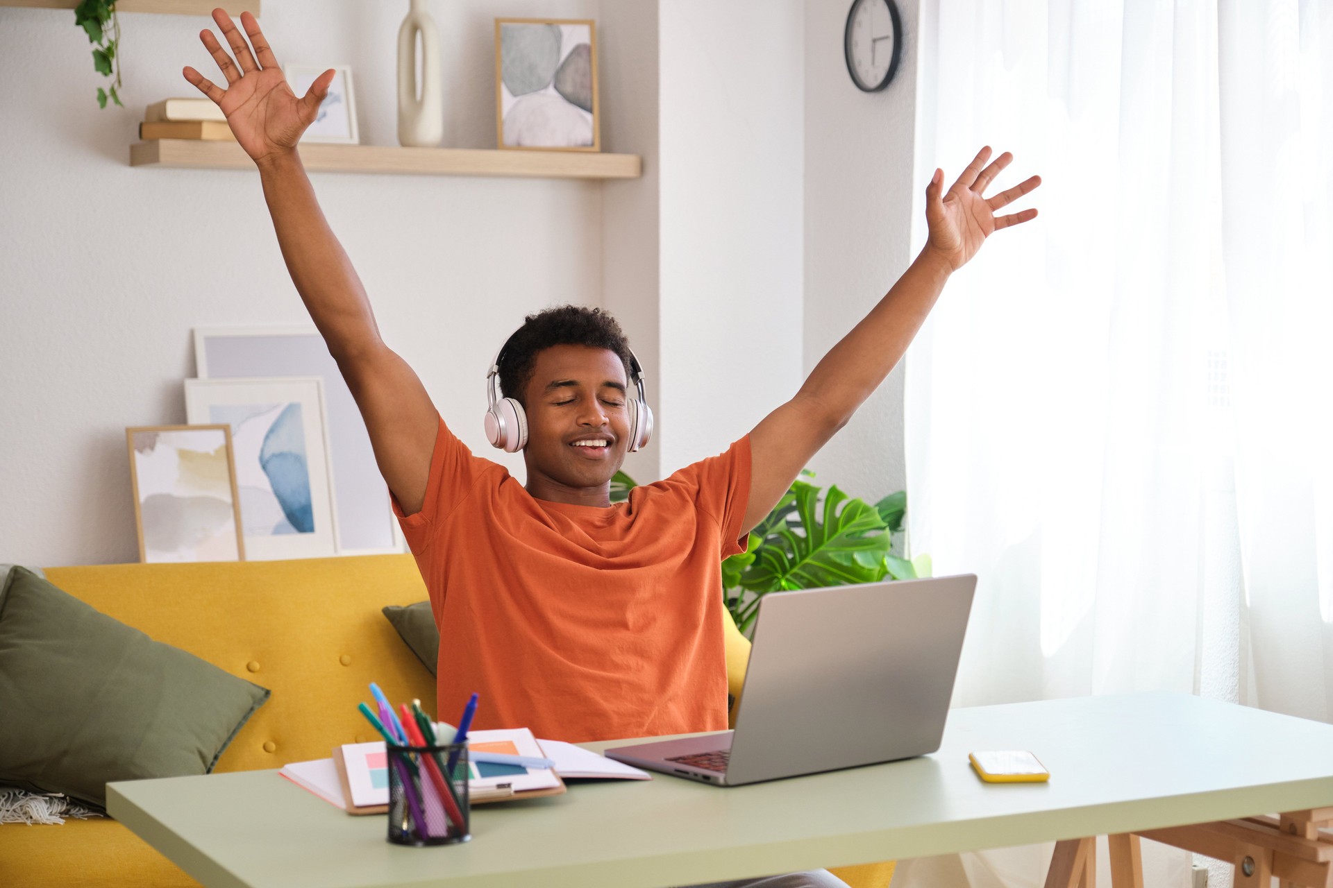 A student man is celebrating passing an exam with his hands raised in the air