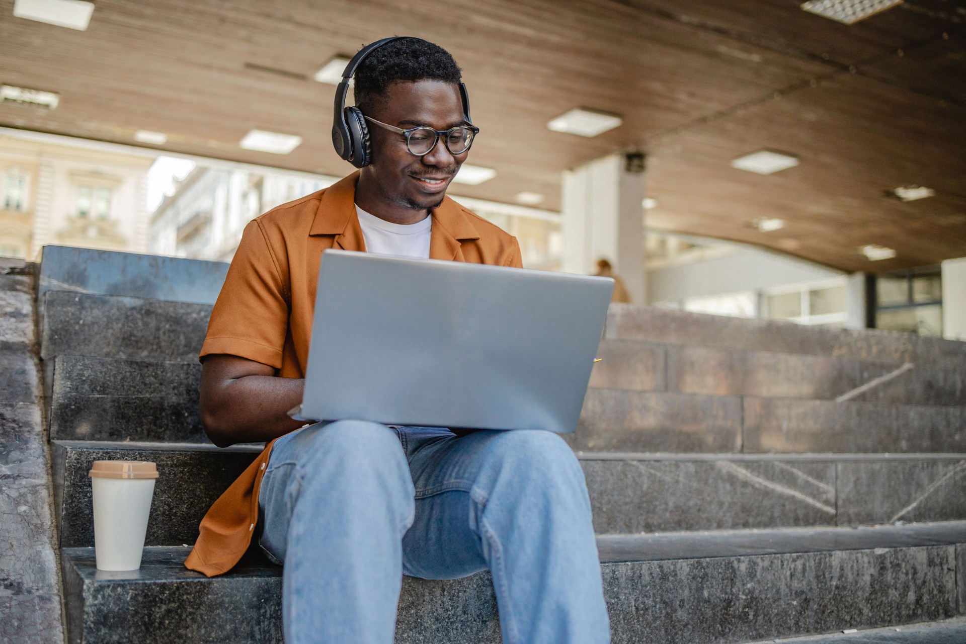 Smart African American student browsing internet via laptop on stairs